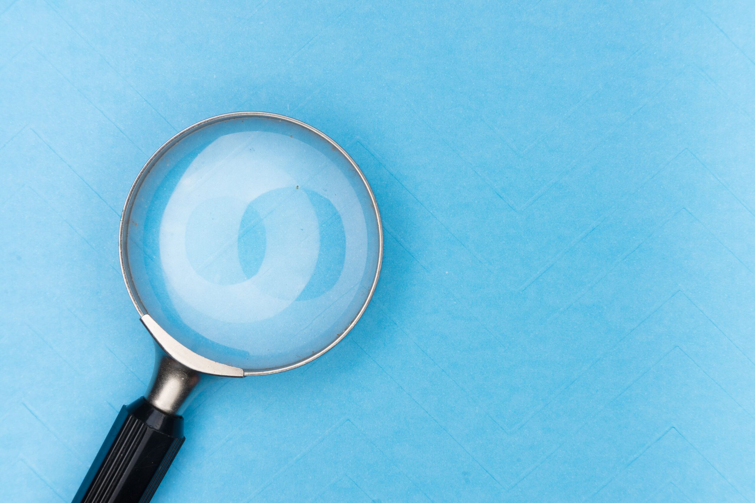 Close-up of a magnifying glass on a blue surface, ideal for search and exploration themes.